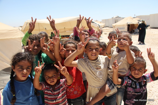 Children pose for the camera holding up the “V” for victory with their fingers. 